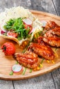 Fried chicken wings with fresh salad, grilled vegetables and bbq sauce on cutting board on wooden background Royalty Free Stock Photo