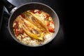 Fried chicory vegetable with tomatoes and feta cheese in a cooking pan on a black stove, copy space
