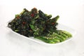 fried cooked green vegetables called kailan are served on a white plate. on solid white background