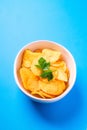 Fried corrugated golden potato chips with parsley leaf in ceramic bowl on blue background