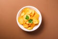 Fried corrugated golden potato chips with parsley leaf in wooden bowl on brown background Royalty Free Stock Photo