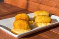 Fried croquettes with yellow cream sauce on white plate at sunny kitchen. Side view on wooden background.