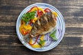 Fried crucian carp with pepper and onion on a plate on a wooden background. Top view