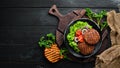 fried cutlet for burger with vegetables. In a black plate on a wooden background Top view. Royalty Free Stock Photo