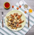 Fried delicious chicken wings with fried potatoes spicy chili sauce and cherry tomatoes seasoned with a fork and knife on a st Royalty Free Stock Photo