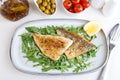 Fried dorado fillet with crispy skin. Arugula, cherry tomatoes, olives, lemon and olive oil. Traditional Mediterranean dish.