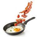 Fried egg bacon and cherry tomatoes flying into iron skillet isolated on white background Royalty Free Stock Photo