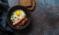 Fried egg, bacon and sausages in a skillet on dark stone background Royalty Free Stock Photo