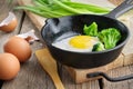 Fried egg with broccoli on a frying pan. Green onion on cutting board