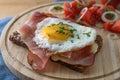 Fried egg and ham on a dark whole meal bread, tomatoes, onion rings and herbs garnish, served on a wooden cutting board