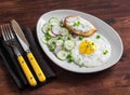 Fried egg, salad with cucumbers, radishes and green peas, toast with feta cheese on a light ceramic plate on dark wooden backgroun Royalty Free Stock Photo