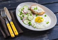 Fried egg, salad with cucumbers, radishes and green peas, toast with feta cheese on a light ceramic plate on dark wooden backgroun Royalty Free Stock Photo