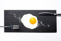 Fried egg on slate plate with knife, fork and salt on white background. Cooking and food concept Royalty Free Stock Photo