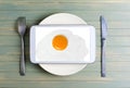 Fried egg on the tablet screen. Cutlery - knife and fork. The tablet computer is on a white round plate. Wooden background Royalty Free Stock Photo