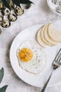 Fried egg on a white plate with a fork for breakfast next to a sliced pear, a tray with quail eggs on a gray concrete background