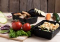 Fried eggplants in container with grilled chicken wings and raw vegetables on rustic background, cherry tomato and micro greenss