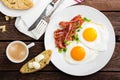 Fried eggs, bacon and italian ciabatta bread on white plate. Cup of coffee. Breakfast. Top view. Wooden background Royalty Free Stock Photo