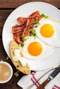 Fried eggs, bacon and italian ciabatta bread on white plate. Cup of coffee. Breakfast. Top view. Wooden background Royalty Free Stock Photo