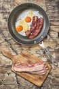 Fried Eggs and Bacon in Teflon Frying Pan with Bacon Rashers on Cutting Board on Old Cracked Peeled Wooden Table Royalty Free Stock Photo