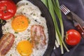 Fried eggs with bacon and tomatoes on an old cast iron pan and cutlery on a gray table. Royalty Free Stock Photo