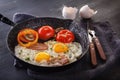 Fried eggs with bacon and tomatoes on an old cast iron pan and cutlery on a gray table. Royalty Free Stock Photo