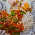 Fried eggs with burnt egg white and irregular seasoning before a portion of rice with fried vegetable strips on a plate on a