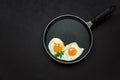 Fried eggs in frying pan with arugula leaves, salt and pepper for breakfast on black wooden background. Top view. Flat lay. Copy