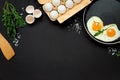 Fried eggs in frying pan with arugula leaves, salt and pepper for breakfast on black wooden background. Top view. Flat lay. Copy Royalty Free Stock Photo