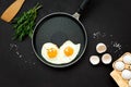 Fried eggs in frying pan with arugula leaves, salt and pepper for breakfast on black wooden background. Top view. Flat lay. Copy Royalty Free Stock Photo