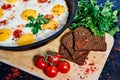 Fried eggs in a frying pan with cherry tomatoes and bread for breakfast on a black background