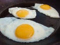 3 fried eggs frying in a pan with olive oil. Three fried eggs in cast iron frying pan sprinkled with ground black Royalty Free Stock Photo