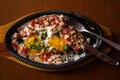 Fried eggs with meat, tomatoes and herbs in an oval plate on a wooden stand