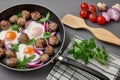 Fried eggs with onions, meatballs and tomatoes, fried in a large frying pan on a gray table Royalty Free Stock Photo