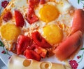 Fried eggs with ripe red cut tomatoes. Dish with rolls of smoked salmon and hard cheese for garnish Royalty Free Stock Photo