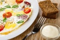 Fried eggs with sausage, tomato in plate, pieces of bread, fork, bowl with mayonnaise on table