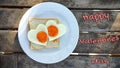 Fried eggs in the shape of a heart at toast on white plate and wooden table. Breakfast with love. Inscription Happy Valentine`s Royalty Free Stock Photo