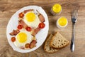 Fried eggs with gammon and cherry tomato in dish, salt and pepper, pieces of bread, fork on wooden table. Top view