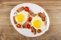 Fried eggs with gammon and cherry tomato in dish on wooden table. Top view