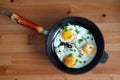 Fried eggs of three eggs on an old cast-iron frying pan standing on a wooden surface top view closeup Royalty Free Stock Photo