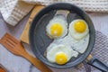 Fried eggs of three eggs in a frying pan on the table on a wooden stand with wooden spatula. Rustic breakfast. Top view. Royalty Free Stock Photo