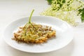 fried elderflower in pancake batter with powdered sugar on a plate on a white wooden table, traditional pastry or dessert