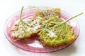 Fried elderflower pancakes with powdered sugar on a pink glass d