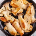 Fried eryngii mushrooms in cast-iron pan on white table. Grilled slices of king oyster mushrooms. Top view, copy space