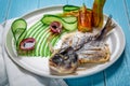 Fried fish dorado, decorated with cucumbers and onions. On a blue wooden background Royalty Free Stock Photo