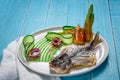 Fried fish dorado, decorated with cucumbers and onions. On a blue wooden background Royalty Free Stock Photo