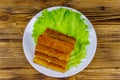 Fried fish fingers on a plate with lettuce on wooden table. Top view