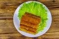Fried fish fingers on plate with lettuce on wooden table. Top view