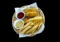 Fried fish and French fries with tomato sauce, cream sauce in the white wicker basket. Royalty Free Stock Photo