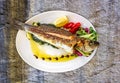 Fried fish with fresh herbs, lemon and vegetables on white plate on a natural stone background