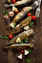 Fried fishes with addition of herbs, spices and lemon slices on a wooden background